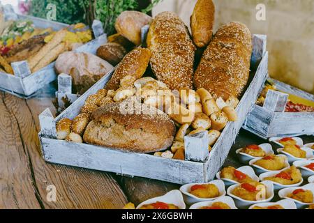 Assortimento di pane rustico e stuzzichini gourmet esposti in casse di legno, splendidamente disposti su un tavolo di legno, che mostra un prodotto da forno pres Foto Stock