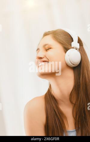 Il suo volto che si illumina alla luce del sole, questa giovane donna con le cuffie trova gioia in una melodia, sentendo profondamente la musica Foto Stock