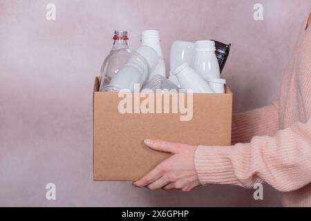 La donna tiene una scatola di cartone piena di rifiuti di plastica Foto Stock