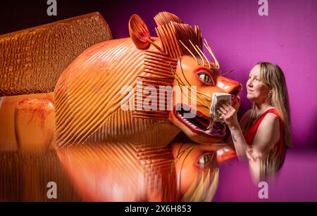 Kat Baxter curatore di archeologia, pulisce una bara a forma di leone (riflessa in un armadietto di vetro) realizzata dal famoso falegname ghanese Paa Joe, noto per la scultura di abebuu adekai, o "proverbi box", che mirano a catturare elementi della vita della persona defunta. La bara fa parte della mostra Living with Death al Leeds City Museum, che esplora i diversi modi in cui le persone sperimentano la morte, la morte e il dolore. Data foto: Mercoledì 15 maggio 2024. Foto Stock