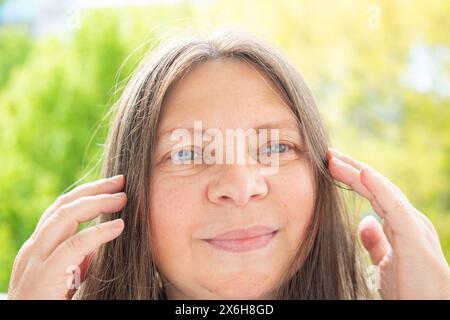 Caucasico positivo donna attraente di 50 anni con capelli lunghi posa graziosamente, bella faccia primo piano ritratto, cura anti-invecchiamento procedure Foto Stock