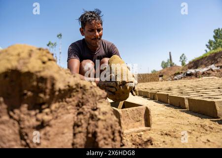 Un operaio non locale usa il fango per creare mattoni usando uno stampo in un forno di mattoni a Budgam. La notevole emissione di elementi tossici dai forni da mattoni rappresenta una grave minaccia per la salute pubblica e l'ambiente. Questi forni rilasciano fumi dannosi che possono influenzare negativamente gli occhi, i polmoni e la gola delle persone esposte a loro. Nel Jammu e nel Kashmir, i problemi di inquinamento dei tradizionali forni di mattoni vengono affrontati con il passaggio alla tecnologia a zig zag. La tecnologia a zig zag introduce un motivo a zig zag nel sistema di cottura del forno. Questo design consente un flusso d'aria più controllato, ottimizzando la combustione Foto Stock