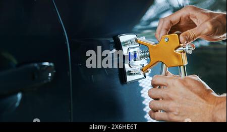 riparazione di ammaccature per auto senza verniciatura. Uomo che fissa la portiera del veicolo con l'attrezzo con tecnologia PDR Foto Stock