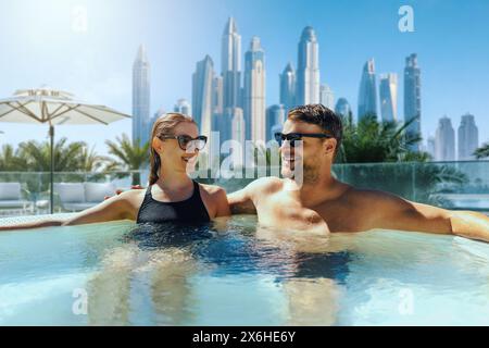 Giovani coppie felici che si rilassano nella vasca idromassaggio all'aperto dell'hotel di Dubai. vacanza di lusso, viaggio breve Foto Stock