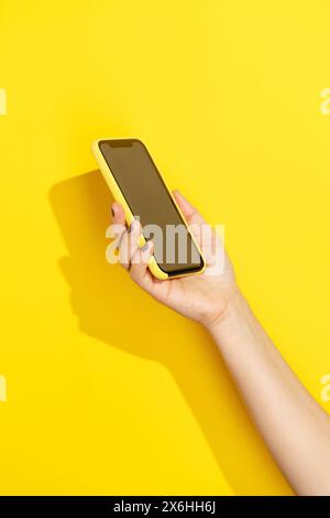 Tenere a mano il telefono con copertina gialla su sfondo giallo Foto Stock