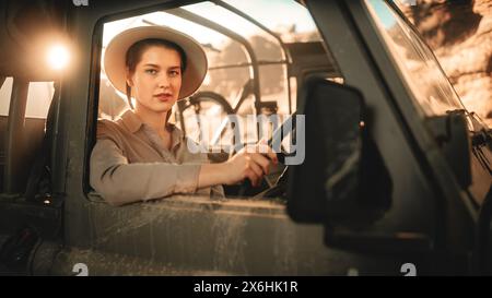 Gita su strada nel deserto: Ritratto di una bellissima esploratrice femminile che guarda fuori dal finestrino dell'autista e sorride. Donna avventuriera che viaggia attraverso il Canyon a bordo del suo SUV fuoristrada. Viaggio attraverso la meravigliosa natura Foto Stock