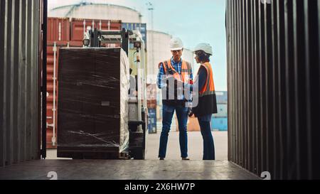 Carrello elevatore a forche caricamento container carico di spedizione con pallet completo con scatole nel terminal porto logistico. Supervisore industriale e ispettore di sicurezza femminile latina con discussione sui tablet, processo di gestione. Foto Stock