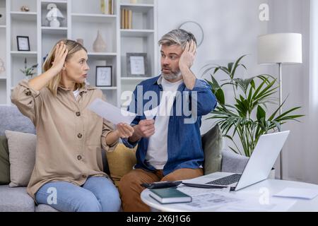 La coppia era stressata, seduta sul divano, a discutere di conti e finanze. Sembrano preoccupati mentre tengono i documenti in mano e si guardano l'un l'altro. Foto Stock