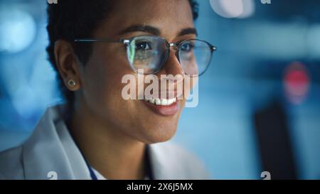 Ritratto dello schermo nero di una donna latina che si riflette nei suoi occhiali. Giovane scienziata intelligente che lavora in laboratorio. Sfondo blu bokeh con luci tecnologiche ad alta tecnologia Foto Stock