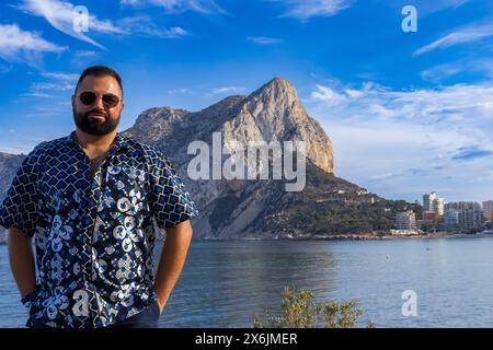 Questo ritratto cattura un uomo di 30 anni mentre si trova in contemplazione, affacciato sull'iconico Penon de Ifach a Calpe, Spagna. Foto Stock