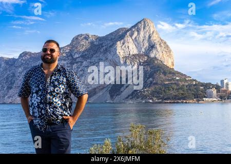 Questo ritratto cattura un uomo di 30 anni in piedi in solitudine contemplativa, con l'iconica roccia di Ifach di Calpe, in Spagna. Foto Stock