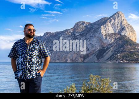 Questo ritratto cattura un uomo di 30 anni mentre si trova in serena contemplazione, con il maestoso monte Ifach di Calpe, in Spagna. Foto Stock