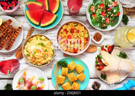 Tavola estiva su sfondo di legno bianco. Varie insalate rinfrescanti, frutta, involtini e spiedini alla griglia. Vista dall'alto. Foto Stock