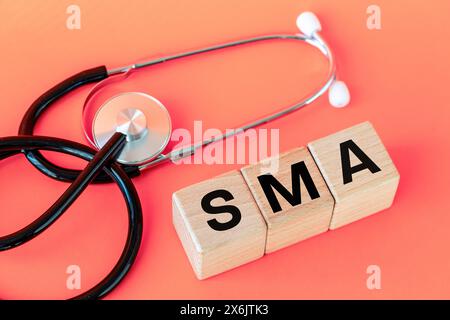 Simbolo di malattia SMA, atrofia muscolare spinale, scritto su blocchi di legno, stetoscopio medico, concetto di salute, copia spazio Foto Stock