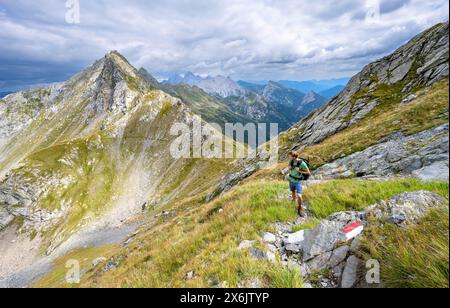 Alpinista su un sentiero escursionistico con segnaletica rossa e bianca, vista della cresta di montagna e della sella Schoenjochl o forca de Fleons, salita a Raudenspitze o. Foto Stock