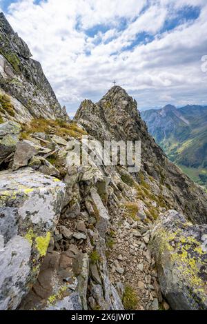 Sentiero di montagna stretto, cima rocciosa a punta del Raudenspitze o del Monte Fleons, con croce sommitale, crinale principale Carnico, Alpi Carniche, Carinzia, Austria Foto Stock