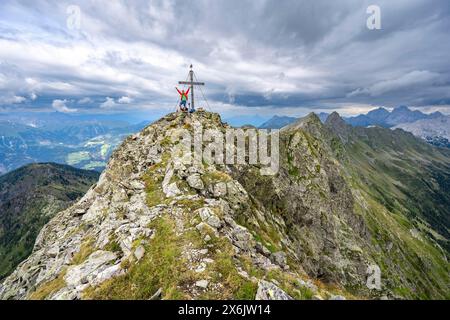 Alpinista stende le braccia in aria, sulla cima rocciosa a punta del Raudenspitze o Monte Fleons con croce sommitale, panorama montano su Foto Stock