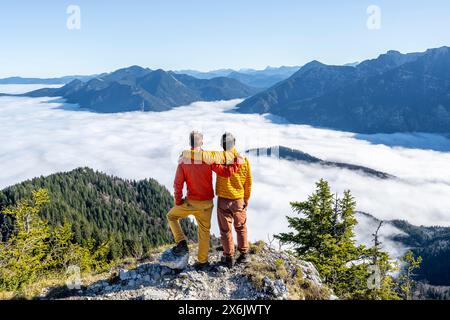 Due amici mettono le braccia l'uno intorno alle spalle dell'altro, gli alpinisti sulla cima rocciosa dell'Ettaler Manndl, la vista sul paesaggio montano e. Foto Stock