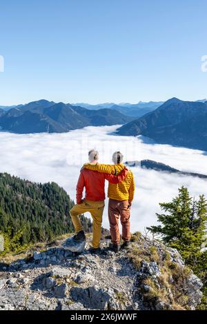 Due amici mettono le braccia l'uno intorno alle spalle dell'altro, gli alpinisti sulla cima rocciosa dell'Ettaler Manndl, la vista sul paesaggio montano e. Foto Stock