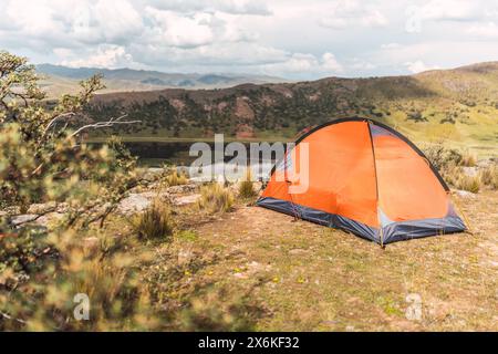 Tenda arancione sulla cima di una montagna con un lago sullo sfondo e cielo blu e nuvole nel mezzo della foresta nella catena montuosa delle Ande Foto Stock