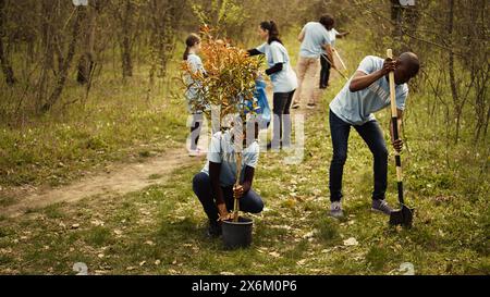 Attivisti ecologici afroamericani piantano piantine in un ambiente forestale, lavorando insieme per preservare e proteggere l'habitat naturale. Progetto Growing Trees. Telecamera B.. Foto Stock