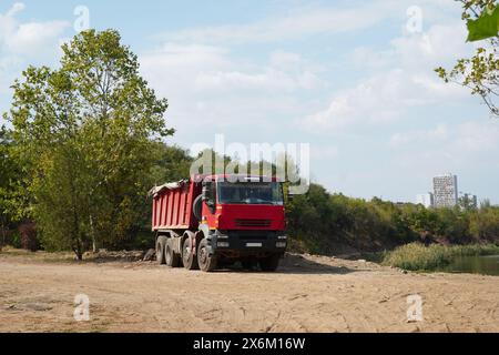 Camion ribaltabile in cantiere, su strada sterrata vicino a alberi e lago, nel quartiere Pantelimon all'interno di Bucarest Foto Stock