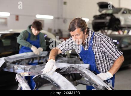 Tecnico esperto della carrozzeria che leviga le parti dell'auto in officina Foto Stock