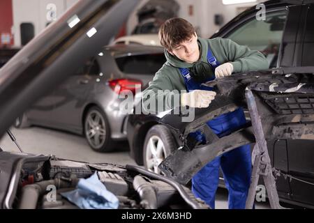 Giovane meccanico specializzato che ripara il paraurti rimosso in officina Foto Stock