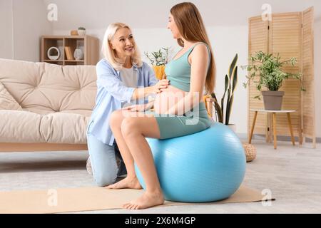 Giovane donna incinta in fitball con doula a casa Foto Stock