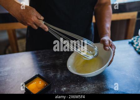 Le mani del panettiere sbattono le uova con un mixer manuale su un piatto bianco, separando i tuorli dai bianchi. Cucinare in modo tradizionale Foto Stock