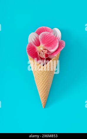 Cono gelato con fiori di orchidea rosa e bianca su sfondo blu acqua. Concept creativo estivo minimalista. Gelato alla moda con l'idea dei fiori. Foto Stock