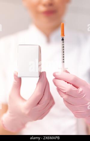 Cosmetologo in guanti rosa che mostra iniezione di sollevamento della pelle e confezione di farmaci mockup. Dermatologo della sfocatura del raccolto in uniforme bianca che dimostra il mockup del prodotto in clinica. Foto Stock