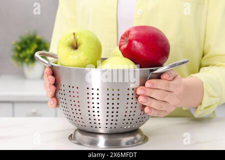 Donna che tiene il colino con mele fresche al tavolo di marmo bianco in cucina, primo piano Foto Stock