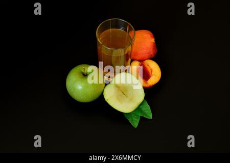 Un bicchiere di succo di frutta appena spremuto su sfondo nero, accanto a mezza mela verde matura e una pesca. Primo piano. Foto Stock