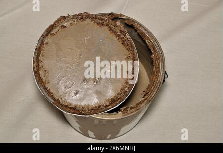 Vecchia scatola per vernice in metallo arrugginito con coperchio aperto su un panno marrone conservazione scaduta. Foto Stock