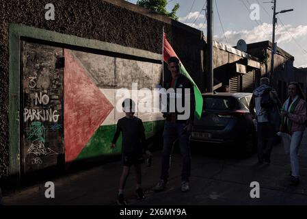 Dublino, Irlanda. 15 maggio 2024. Un ventilatore sventola la bandiera palestinese fuori dall'ingresso dello stadio, di fronte a una seconda bandiera palestinese dipinta sul muro. I tifosi hanno partecipato alla partita di calcio Bohemians-Palestine al Dalymount Park Stadium, che si è svolta a Dublino oggi, 15 maggio, per celebrare il 76° anniversario di Nakba e per mostrare solidarietà alla Palestina. Credito: SOPA Images Limited/Alamy Live News Foto Stock