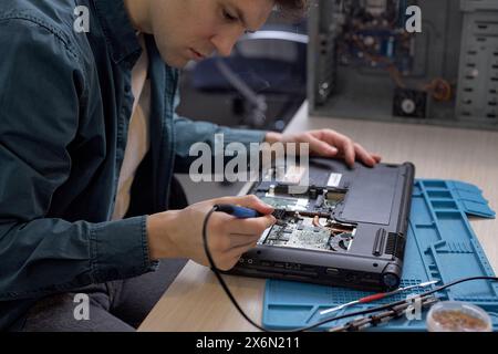Un tecnico professionista ripristina il notebook utilizzando vari strumenti speciali. Officina di riparazione elettronica, rinnovo tecnologico, affari, riparazioni concettuali. ma Foto Stock