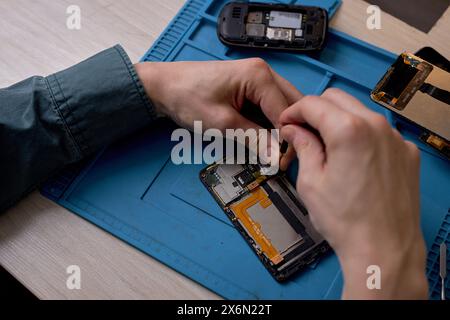 primo piano delle mani del riparatore tagliato svitando le viti dalla custodia dello smartphone con un cacciavite per la riparazione e la manutenzione. riparazione e manutenzione di telefoni cellulari. messa a fuoco selettiva. vista dall'alto Foto Stock