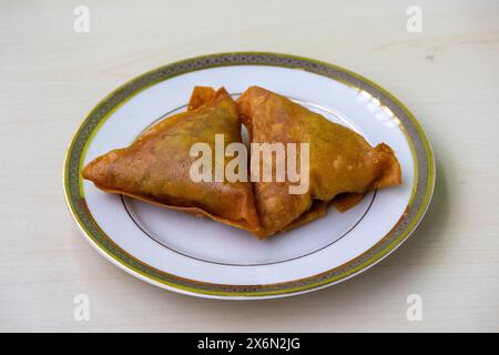 Due samosa su un piatto bianco. Delizioso cibo asiatico con un ripieno saporito, che include ingredienti come patate speziate, cipolle, piselli, carne o pesce. Foto Stock