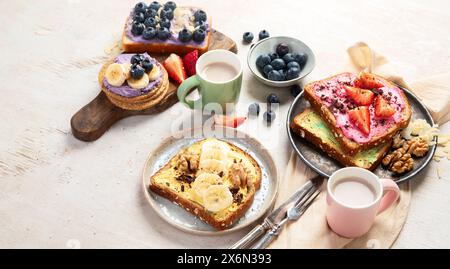 Assortimento di toast dolci. Banana, formaggio spalmabile, burro di arachidi e fragole, formaggio spalmabile e mirtillo su sfondo bianco. Vista dall'alto. Foto Stock