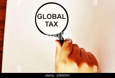 Lente d'ingrandimento sopra il mucchio di soldi con il testo "Global Tax". Concetto della nuova tassa europea. Foto Stock