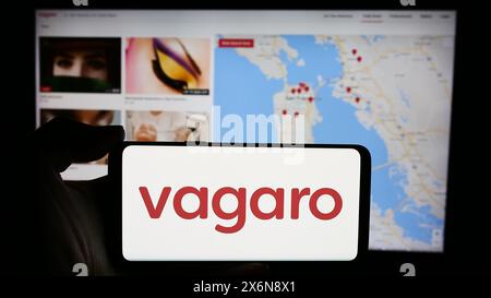 Persona che possiede un telefono cellulare con il logo della società americana di mercato online benessere Vagaro Inc. Davanti alla pagina web. Mettere a fuoco il display del telefono. Foto Stock