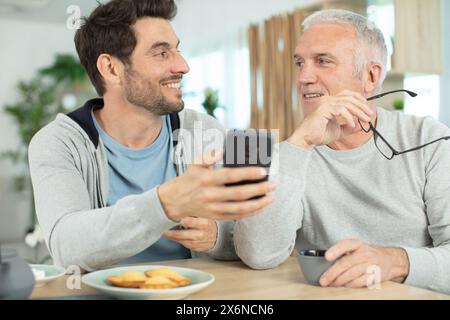 papà anziano e figlio adulto entusiasti che navigano su internet su smartphone Foto Stock