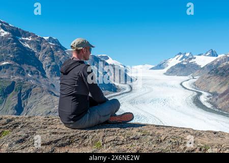 Giovane turista di sesso maschile in costume da trekking con vista sul ghiacciaio Salmon lungo la Cassiar Highway, British Columbia, Canada. Concetto di persone e turismo. Foto Stock