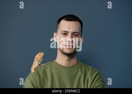 Ritratto minimale di un giovane uomo con iguana gialla sulla spalla che guarda la fotocamera Foto Stock