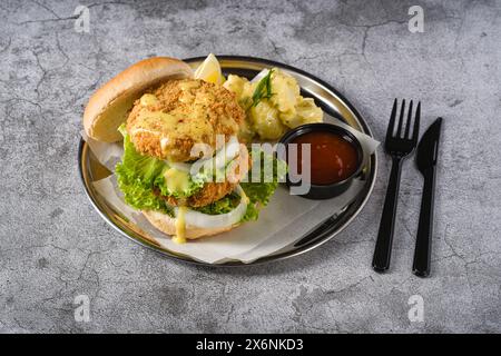 Doppio hamburger di pesce con insalata di patate su un piatto di metallo Foto Stock