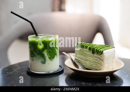 Il tè verde Matcha, il cibo dolce e le bevande sono serviti al caffè, la torta a strati di crepe verde verde e il primo piano del tè verde con latte freddo sul tavolo. Foto Stock