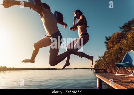 La madre single con suo figlio si diverte in vacanza saltando dal molo il giorno d'estate nel lago. Foto Stock