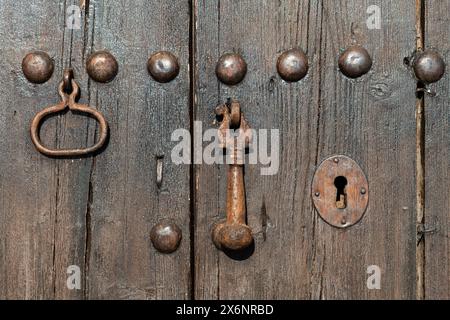 Dettaglio di una vecchia porta in legno ruvido, con rivetti metallici, buco a chiave e battitoio. Foto Stock