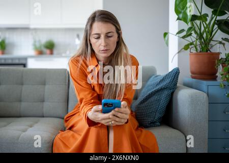 Donna stressata guarda lo schermo dello smartphone, donna triste che legge notizie spiacevoli sul telefono cellulare. Foto Stock